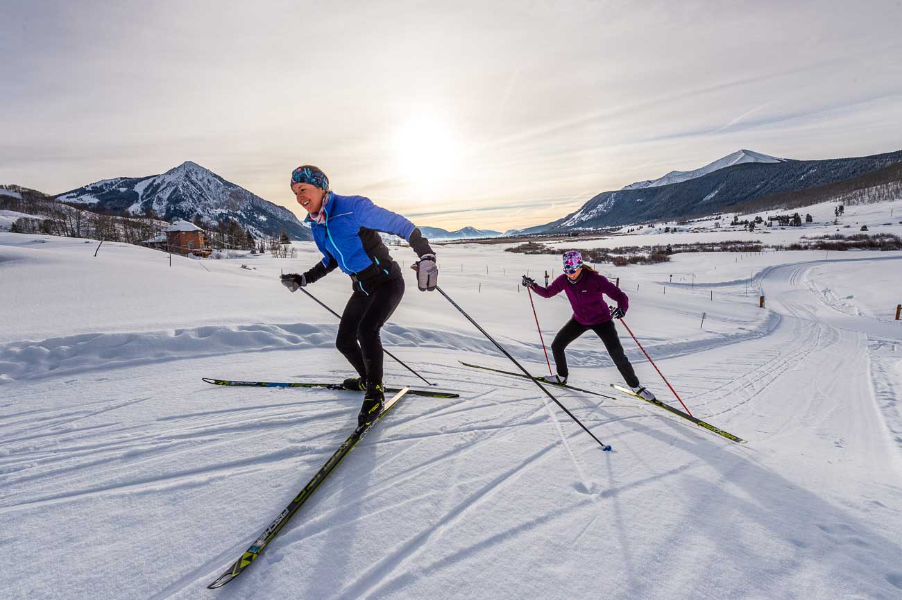 Two nordic skiers racing down the trail at Crested Butte with the sun setting in the background