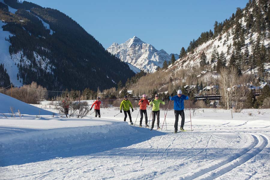 Group of skiers on trails at Aspen Nordic with mountains in background